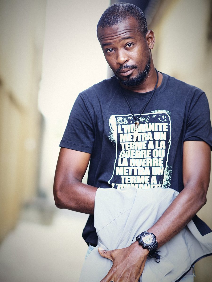 Despy en t-shirt noir, regard vers l'objectif, dans une ruelle